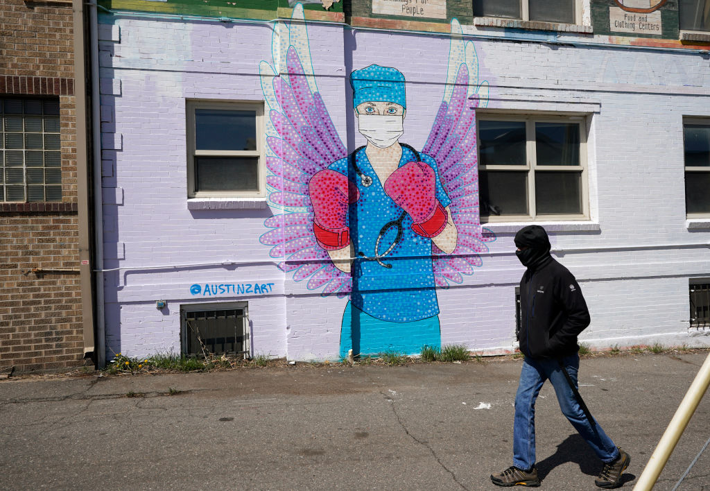 A man in a mask walks by a mural depicting a medical worker with a mask covering her mouth and nose, wearing boxing gloves and angel-like wings on her back on April 14, 2020 in downtown Denver.
