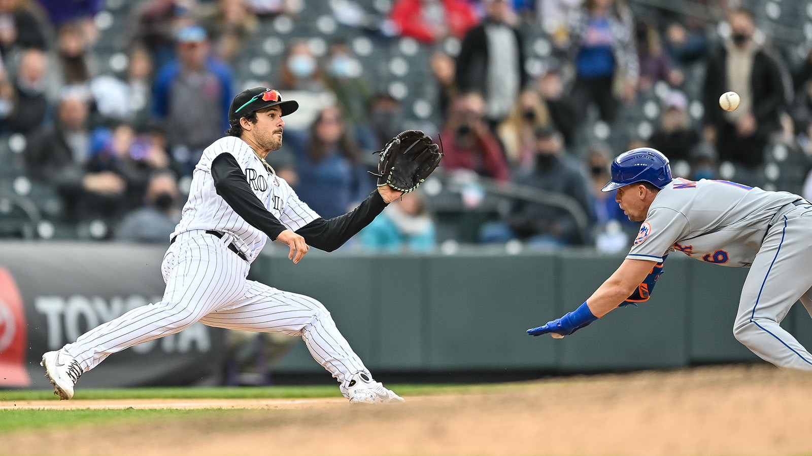 Colorado third baseman Josh Fuentes waits for the throw before tagging out Jeff McNeil attempting to stretch a double during a game between the Rockies and the Mets at Coors Field on April 18, 2021.