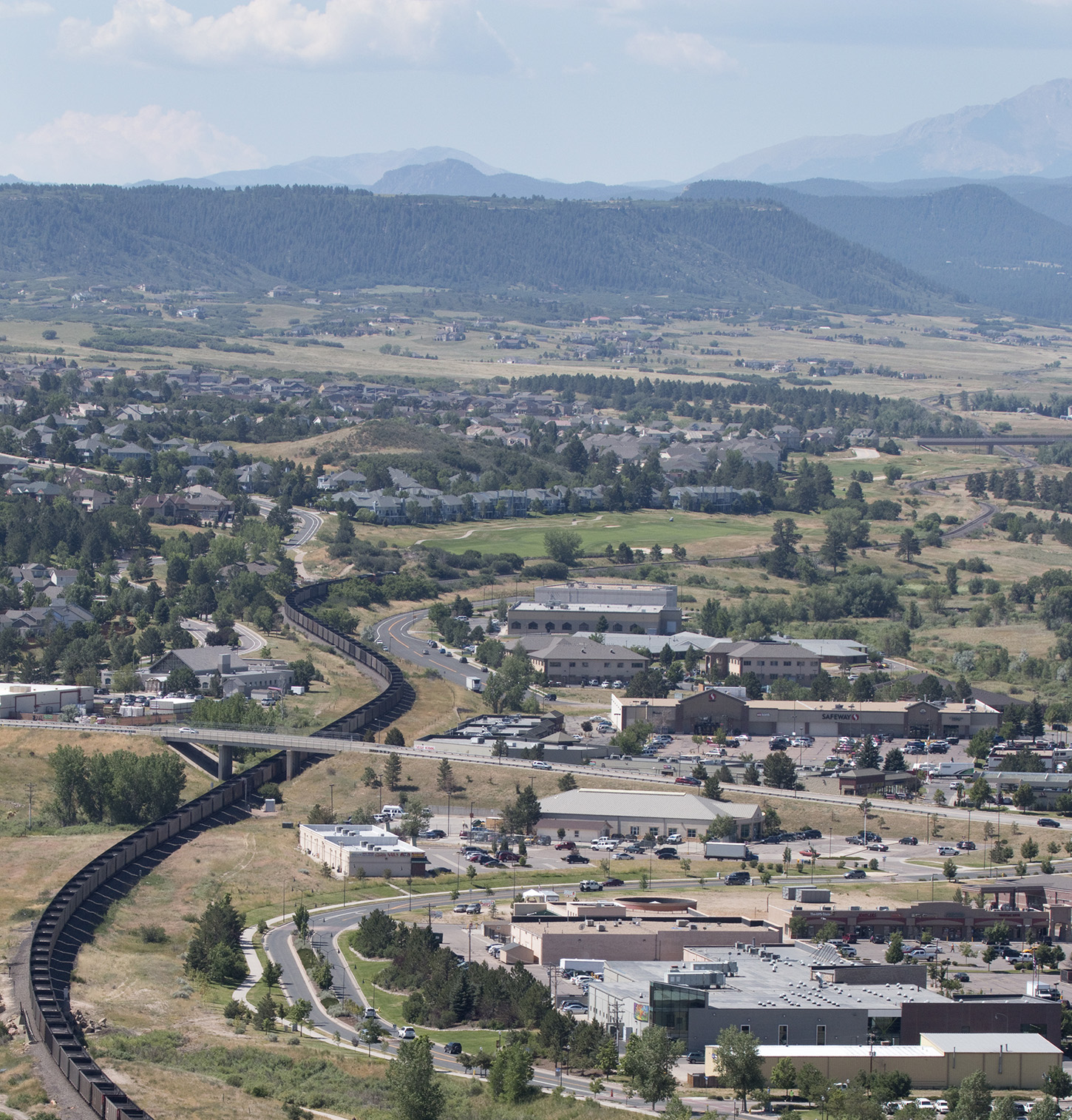 A long, empty coal train snakes through the town Castle Rock, Colorado past homes and businesses with Pikes Peak and the Rocky Mountains in the distance.